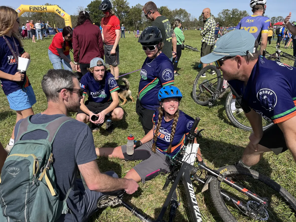 Coaches and teammates chat with a smiling rider after a race.